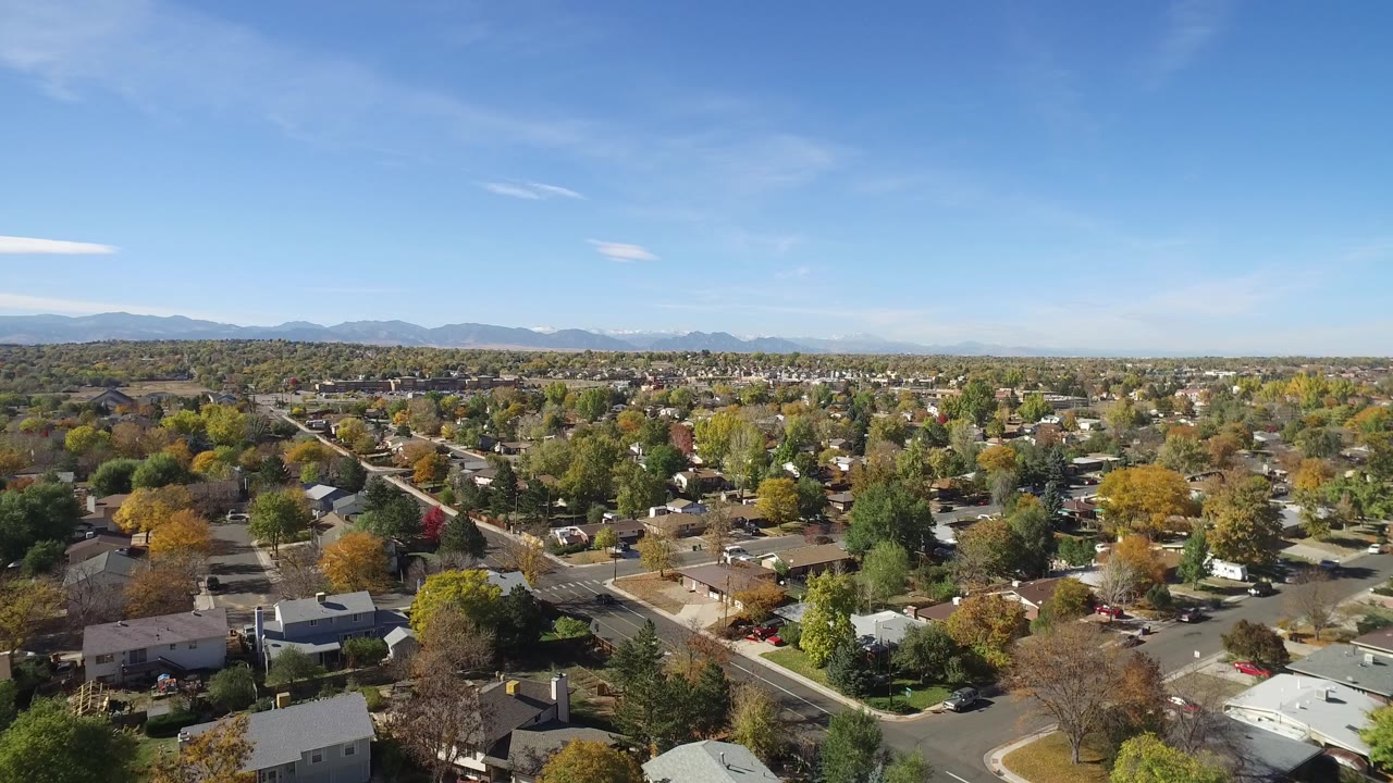 Wide aerial frame over Hidden Lake, Colorado, showing residential streets, detached homes, autumn trees, distant mountains, and no clearly visible people.