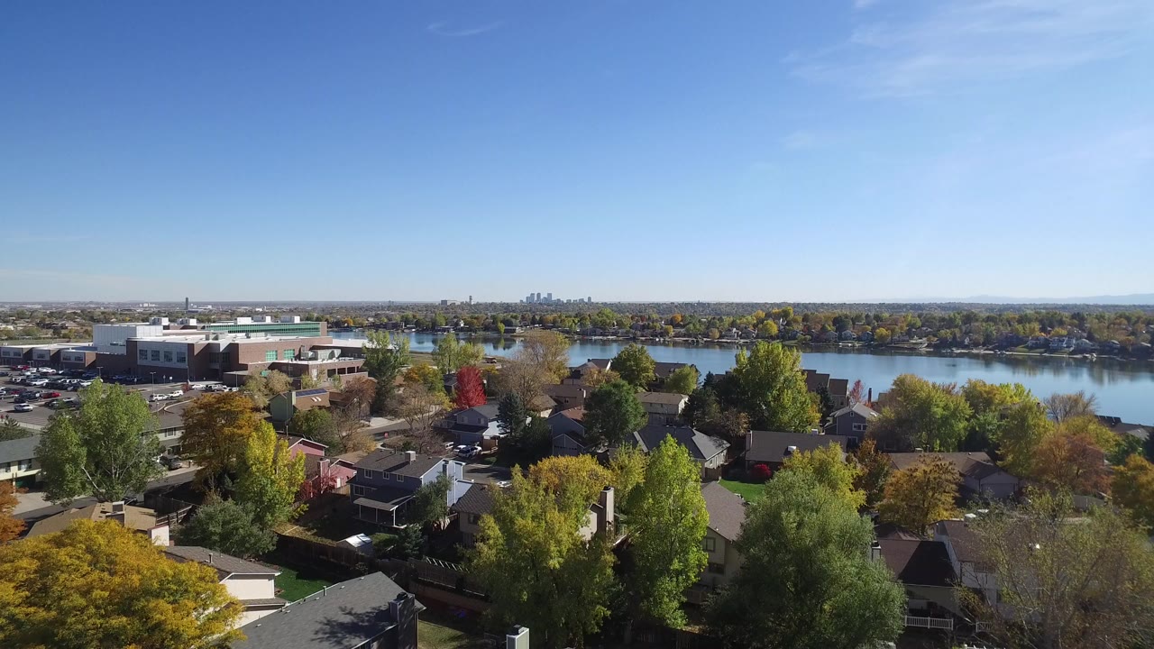Aerial view in Hidden Lake, Colorado with rooftops and autumn trees in the foreground, a broad river or lake behind them, and no visible people.