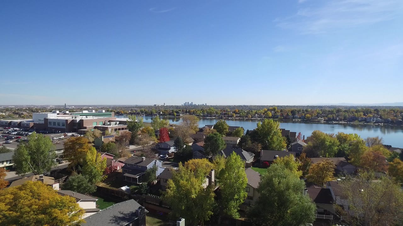 Hidden Lake, Colorado aerial frame showing private homes below, yellow and red autumn trees, parked cars, water in the midground, and no visible people.