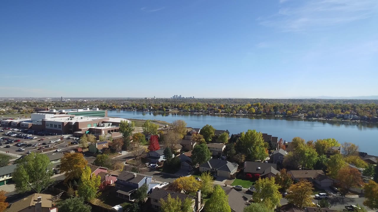 Aerial view in Hidden Lake, Colorado with the large building left of center, residential roofs below, lake across the middle distance, skyline on the horizon, and no visible people.