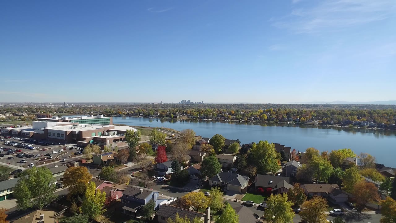 Drone-like aerial over neighborhood beside a lake with trees and skyline beyond