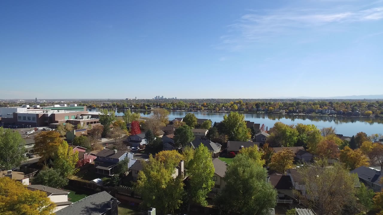 Rooftops and autumn trees beside a calm lake.