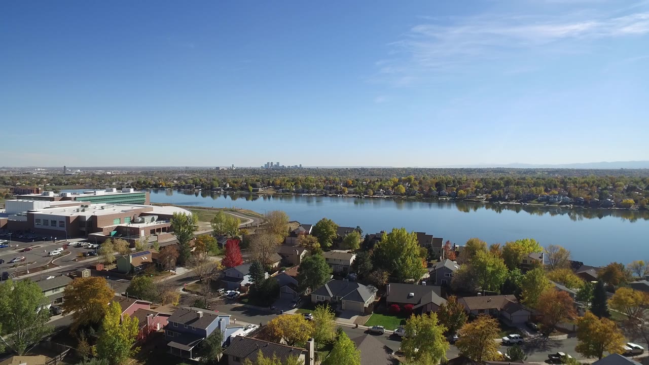 Drone view across a neighborhood and lake under a clear blue sky.
