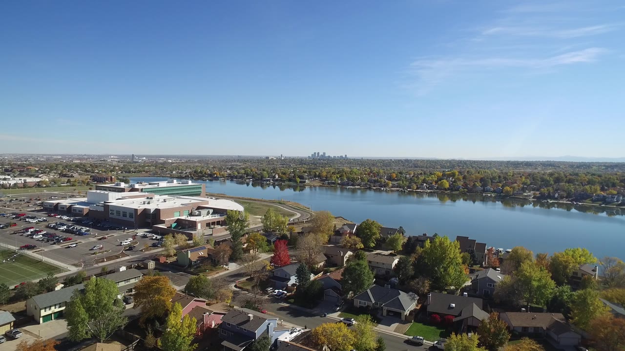 Aerial shot of a lakeside district with rooftops, trees, and open blue sky