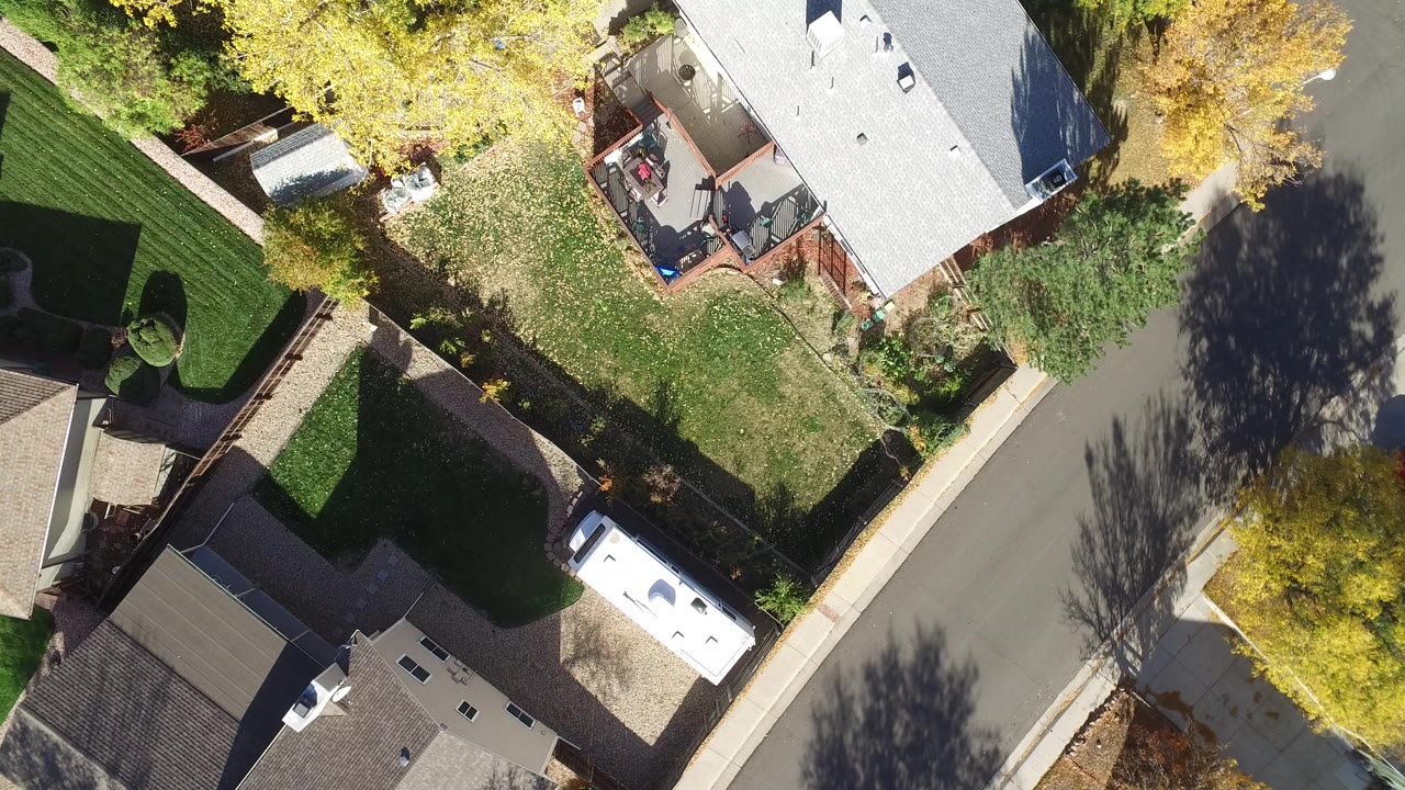 Top-down aerial view of houses, lawns, trees, and a curving street.