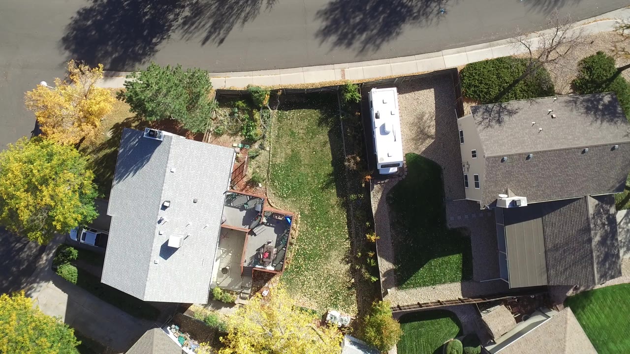 Top-down aerial view of two neighboring houses and yards beside a curved street.