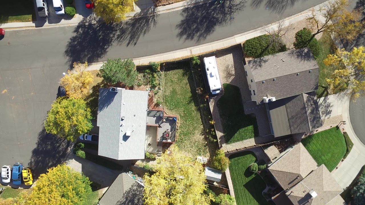 Top-down aerial view of houses, lawns, trees, and a curved residential street.