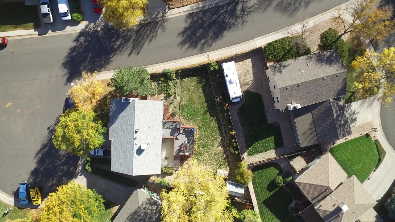 Overhead view of houses, streets, parked vehicles, lawns, and trees.