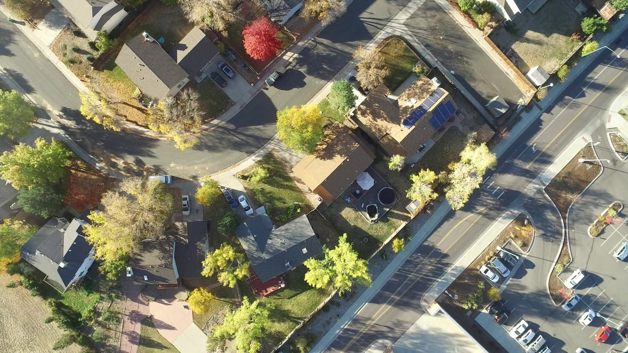 Top-down aerial frame over Hidden Lake, Colorado showing narrow residential streets, detached homes, lawns, driveways, parked cars, fall-colored trees, and no visible people.