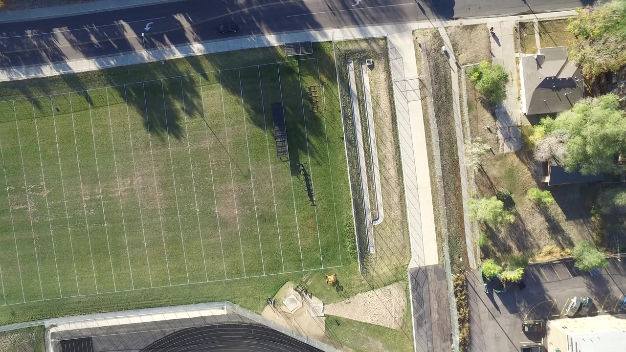Top-down aerial frame in Hidden Lake, Colorado showing a marked football field, a road along the top edge, trees, sidewalks, nearby buildings, and no visible people.