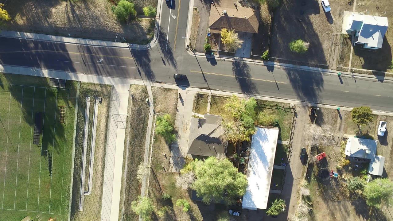 Overhead road with houses, trees, vehicles, and a fenced green field edge.