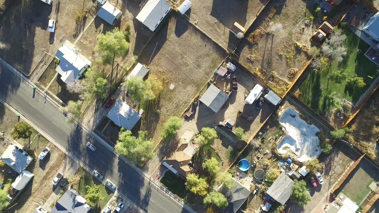 Top-down aerial view of homes, streets, trees, fenced yards, and parked vehicles.