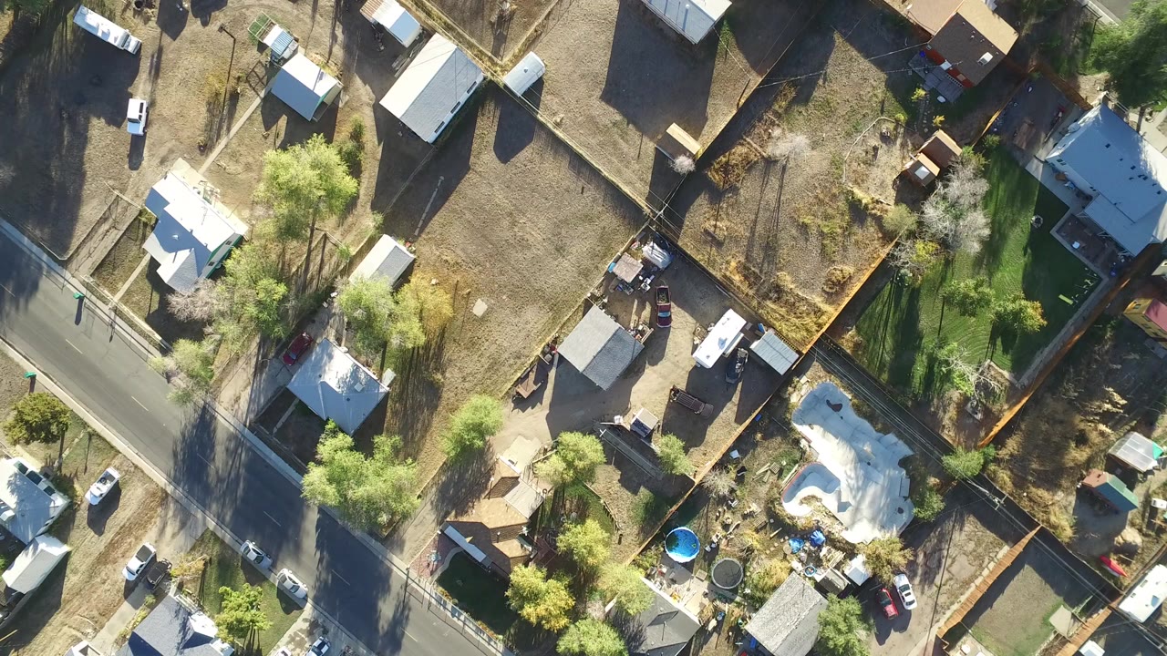Overhead view of houses, fenced yards, trees, and a road.
