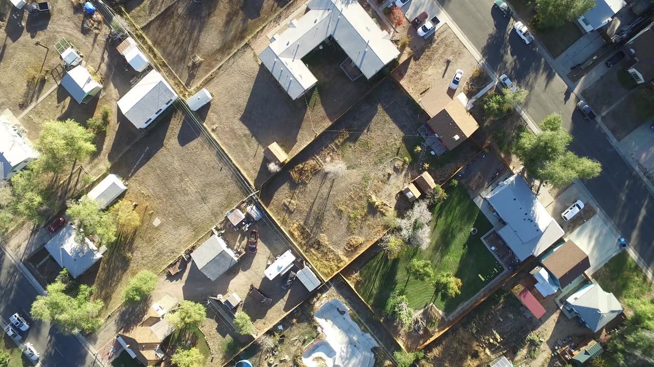 Overhead aerial view of houses, fenced yards, trees, and streets in bright sun.