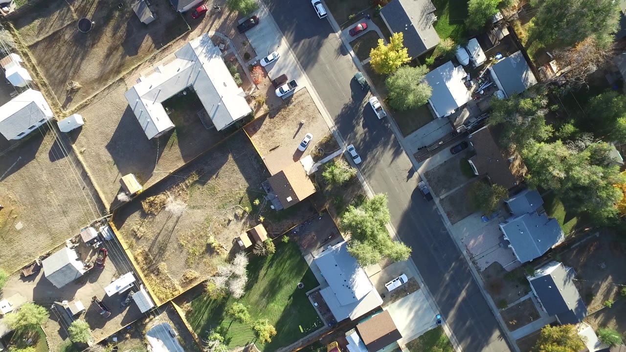 Top-down neighborhood view with homes, trees, cars, and backyards.