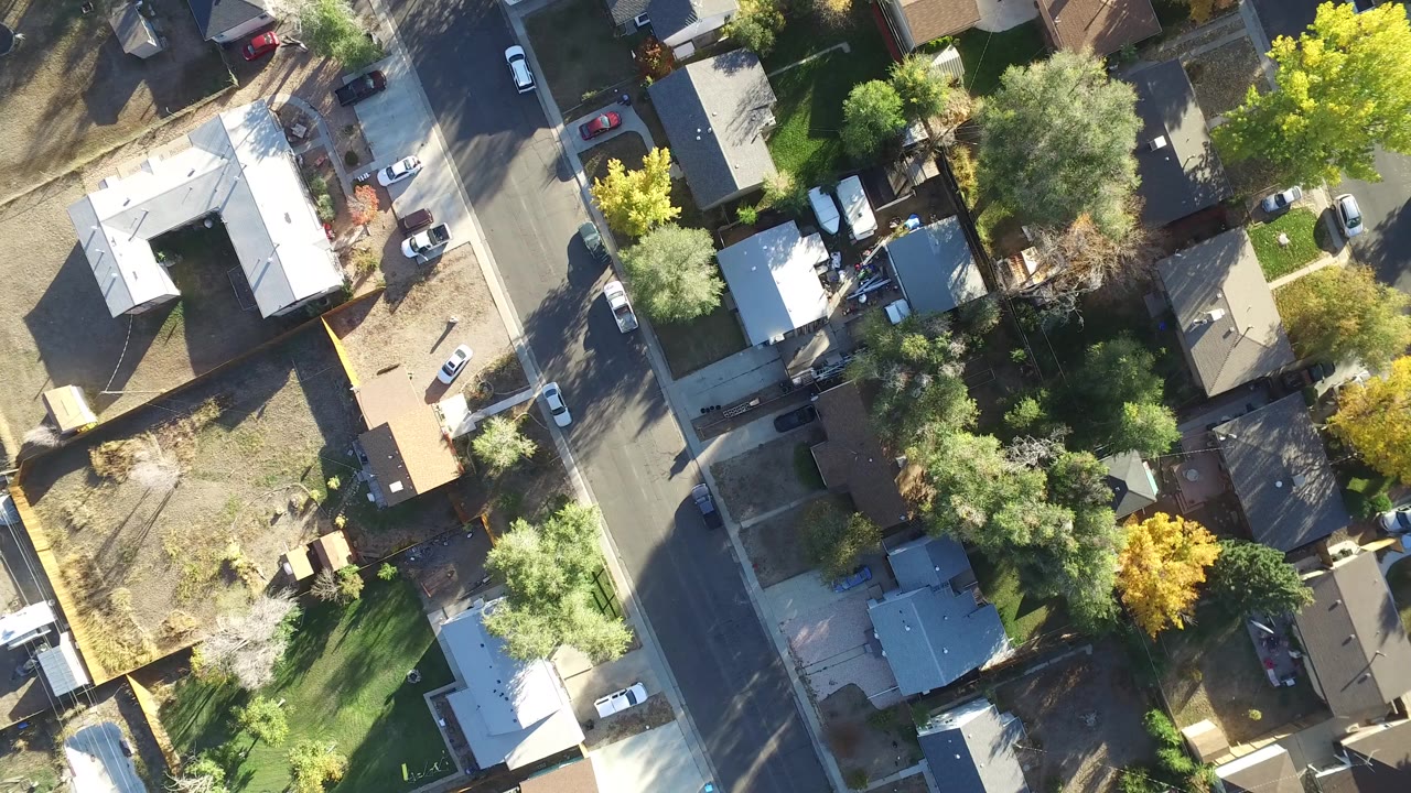 High overhead aerial frame of Hidden Lake, Colorado homes, intersecting residential streets, lawns, parked cars, and green and yellow trees, with no visible people.