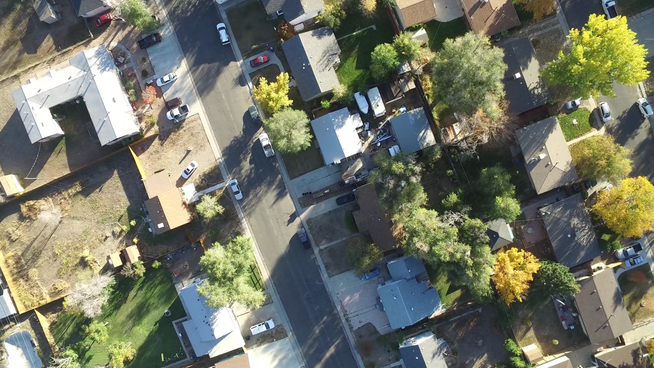 Top-down neighborhood view with houses, driveways, trees, and cars along a street.