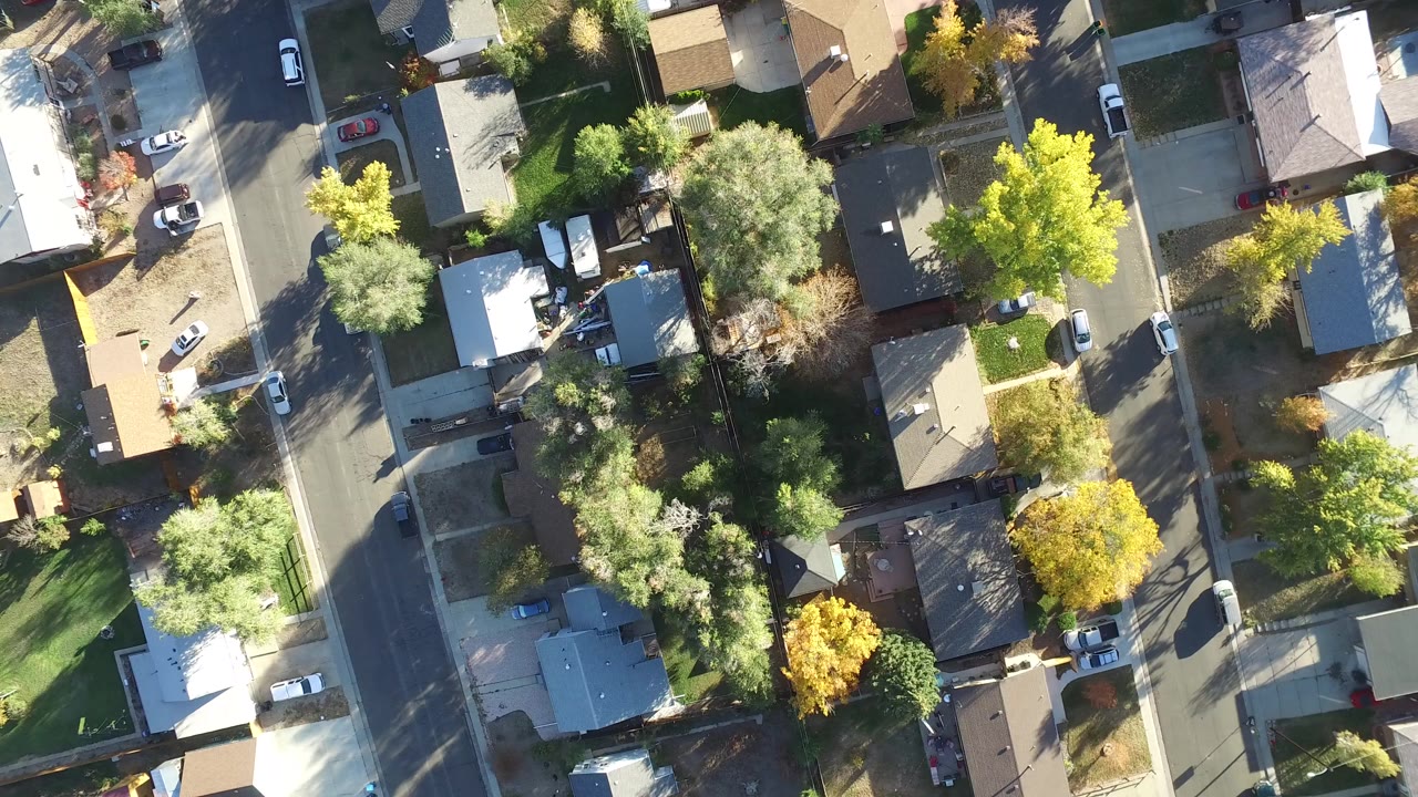 Overhead suburban block with houses, streets, trees, lawns, and parked cars.
