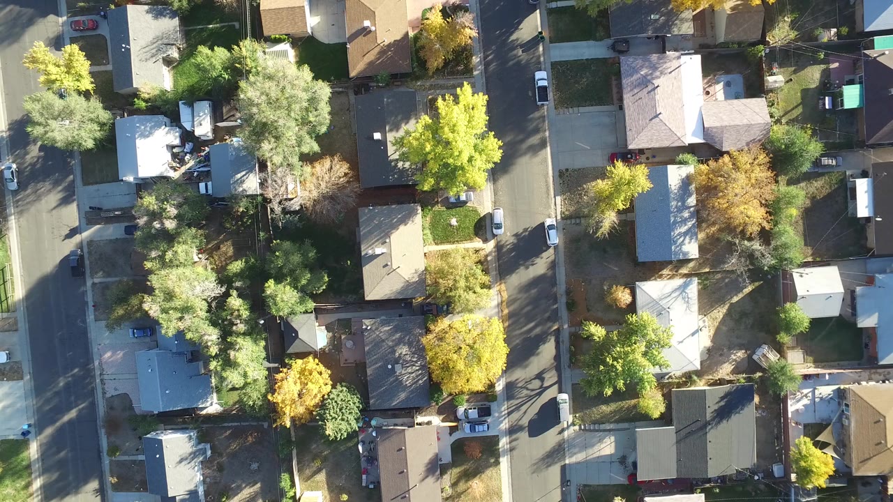 Top-down aerial view of houses, streets, trees, and parked cars.