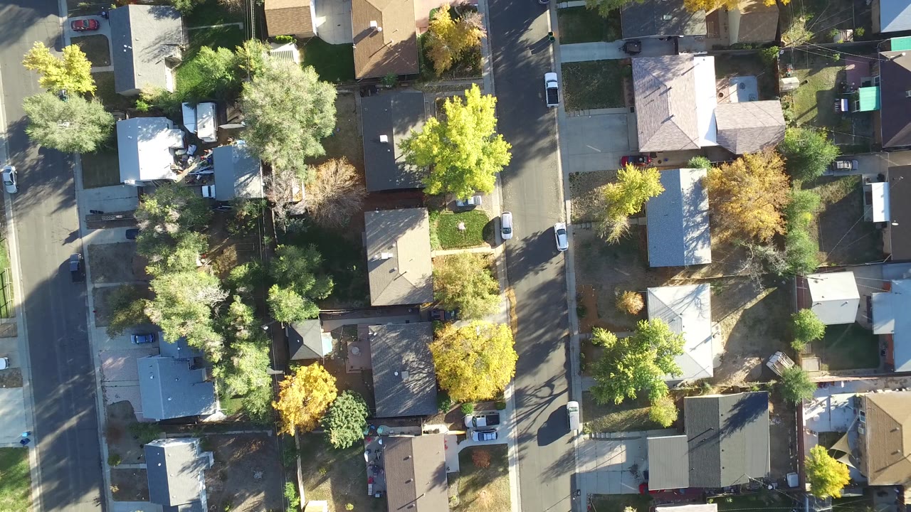 Aerial view in Hidden Lake, Colorado with a pale-roofed house near center, green and yellow trees around the lots, parked cars along the street, and no visible people.