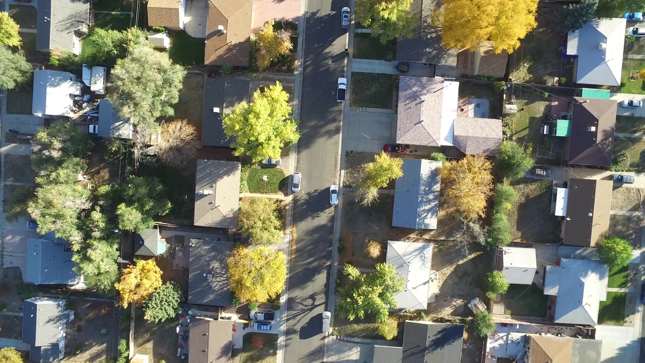 Overhead view of suburban rooftops, streets, trees, and parked cars.