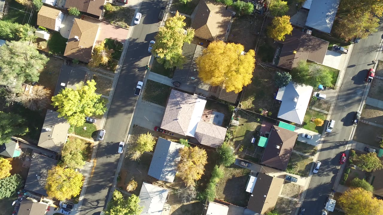 High overhead view of Hidden Lake, Colorado houses, paved streets, driveways, parked cars, and yellow-green fall trees at the start of the clip, with no visible people.