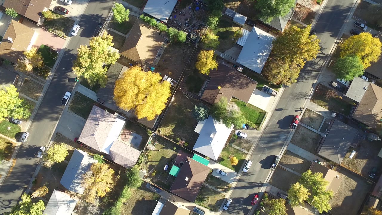 Top-down aerial frame of Hidden Lake, Colorado showing residential rooftops, narrow streets, parked cars, yards, and green and yellow trees, with no visible people.