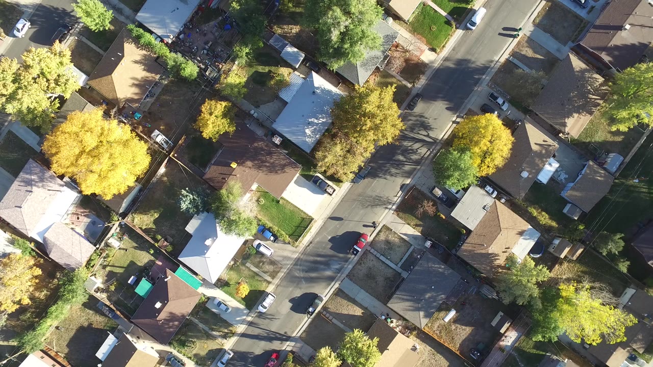 Near-vertical aerial frame over Hidden Lake, Colorado showing rooftops, fenced yards, driveways, leafy trees, and a road crossing the right side with no visible people.