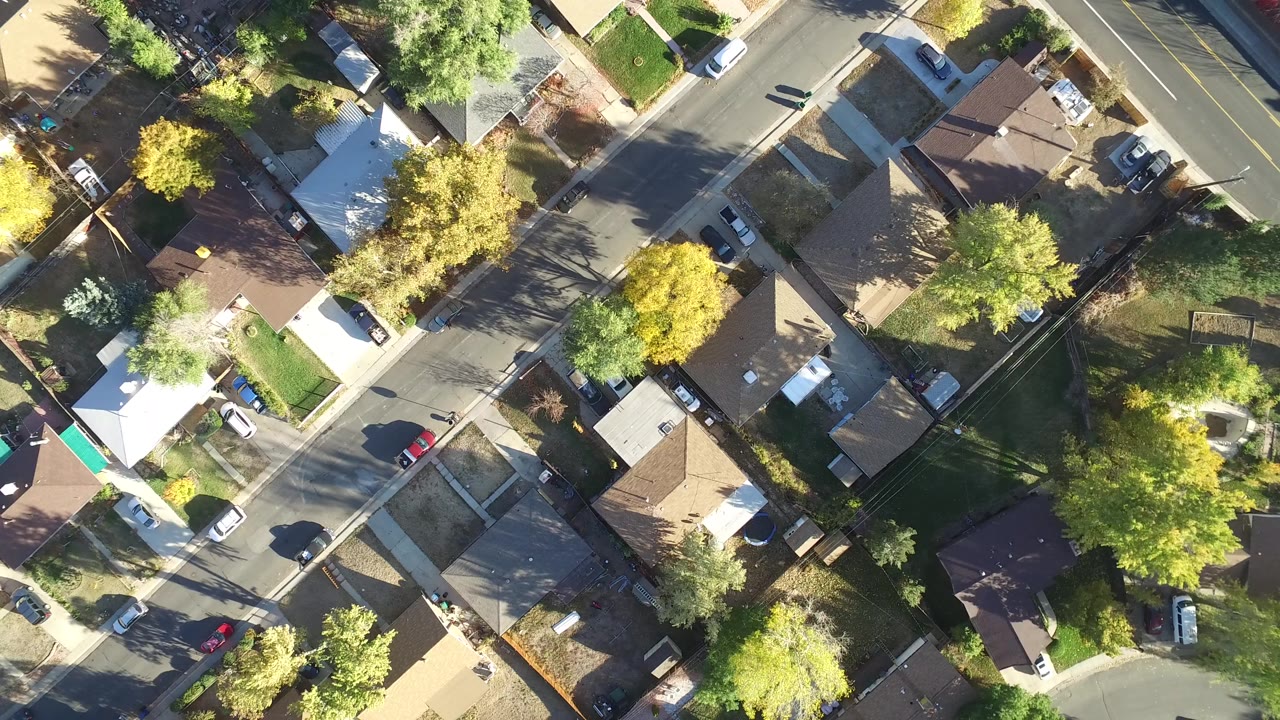 Top-down aerial view of houses, streets, trees, and parked cars.