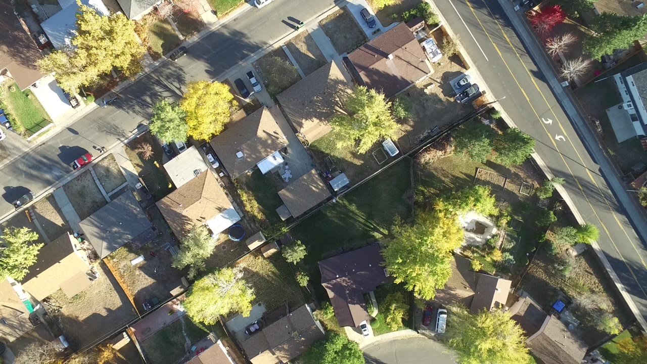 High overhead frame in Hidden Lake, Colorado showing residential roofs, a red parked car, mature trees, driveways, and the road continuing vertically at right with no visible people.