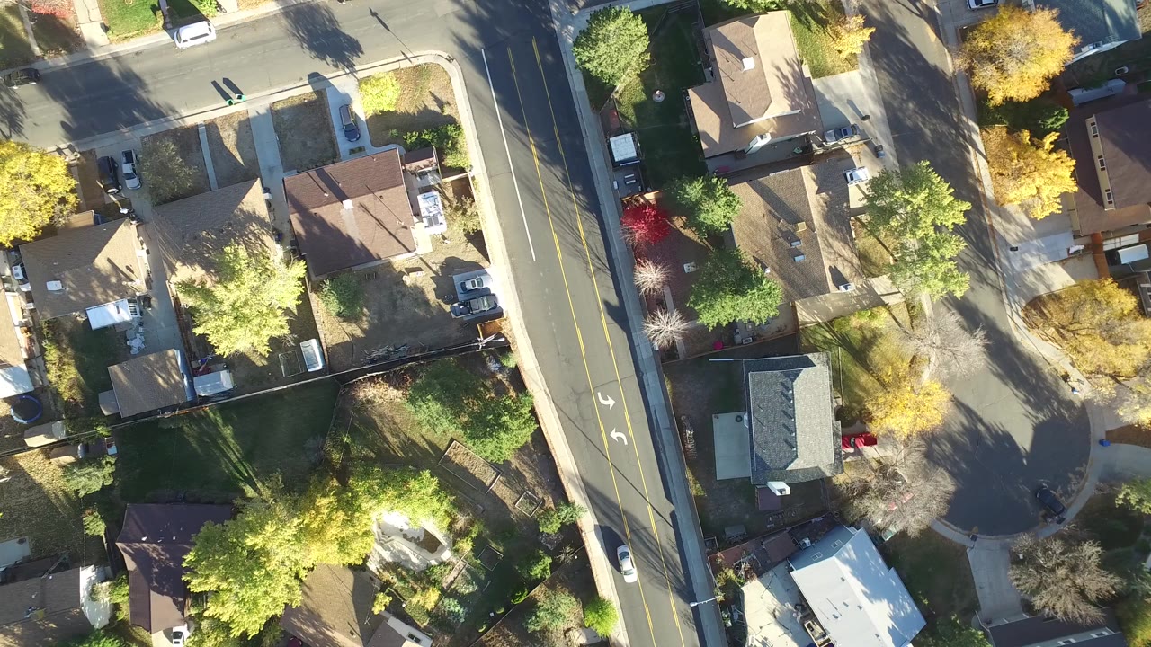 Overhead view of a residential street, houses, trees, and parked cars.