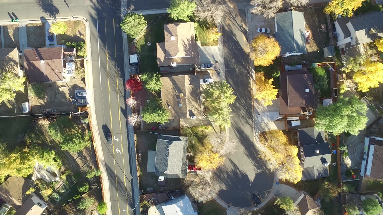 Aerial frame over Hidden Lake, Colorado showing rooflines, driveways, parked vehicles, a curved residential street, and autumn tree cover with no clearly identifiable people visible.