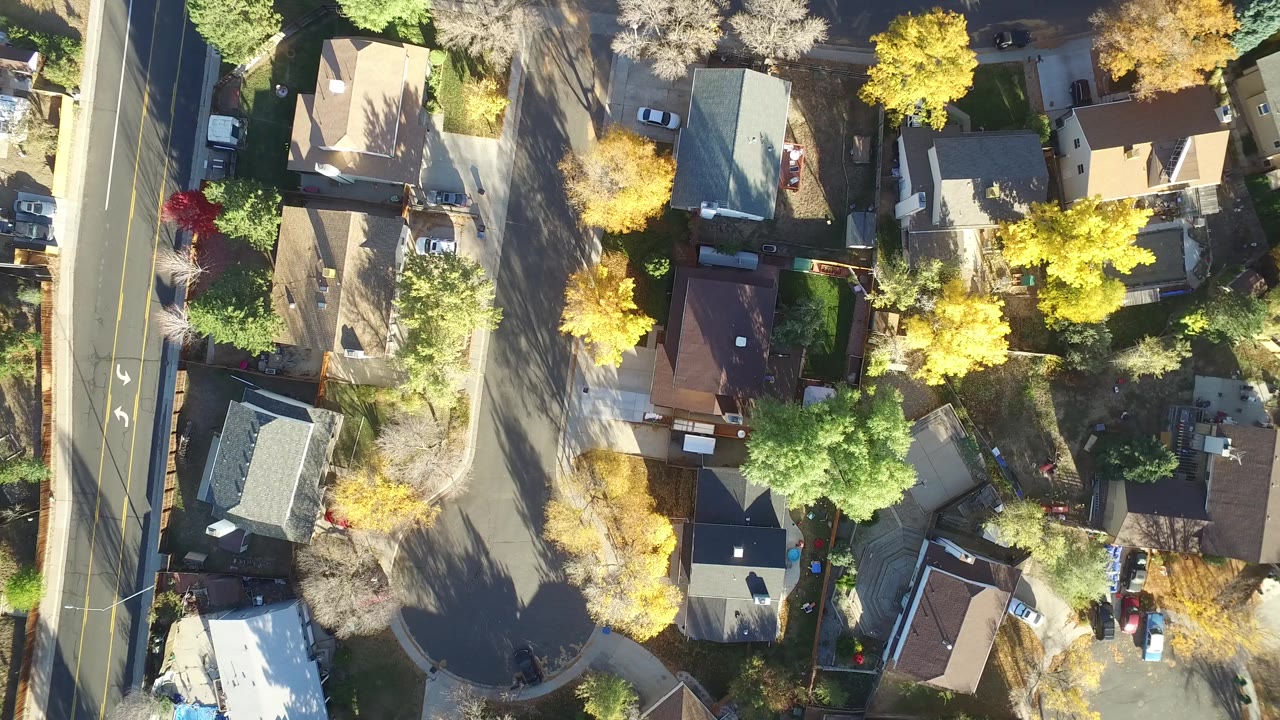 Top-down aerial view of houses, streets, cars, lawns, and trees.