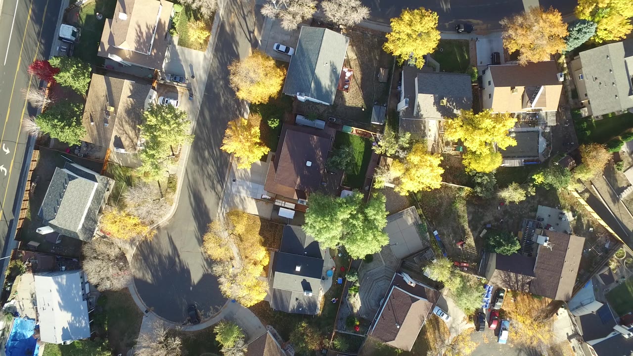 Top-down aerial view of homes, streets, cars, and autumn trees.