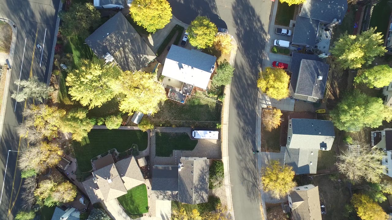 Near-vertical aerial frame in Hidden Lake, Colorado, with rooftops centered among autumn-colored trees, driveways, a white vehicle, and the residential street at right with no visible people.