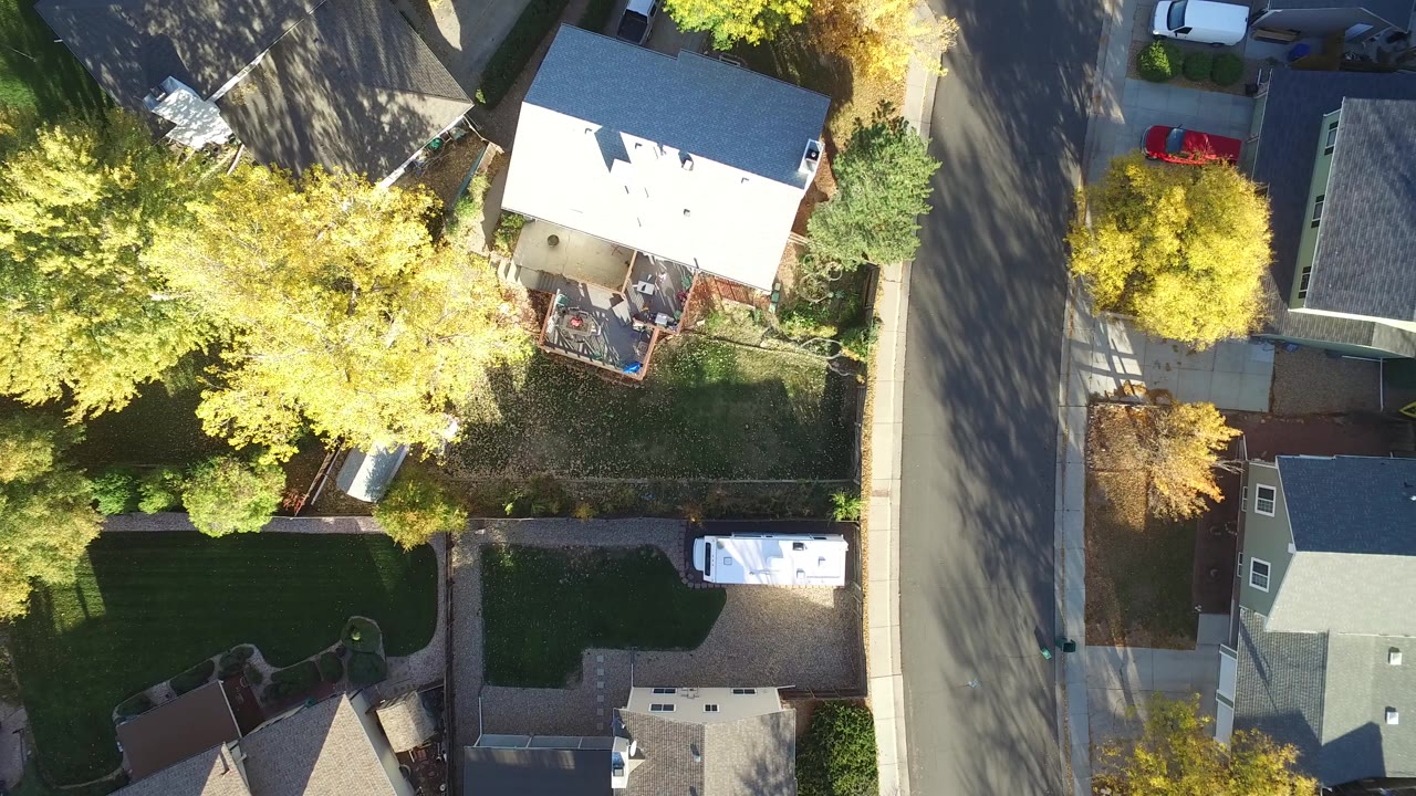Overhead view of houses, yards, trees, and a residential road.