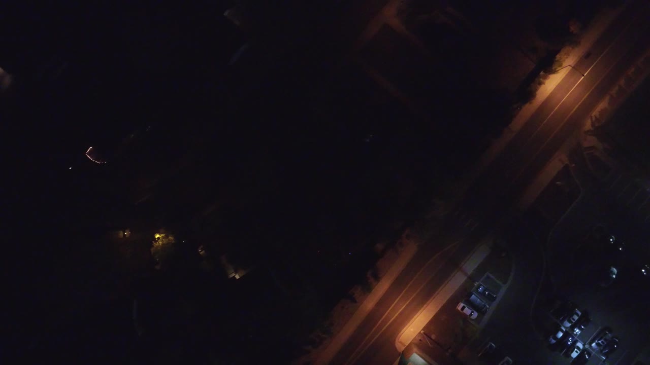 Dark aerial view of a lit residential road at night.