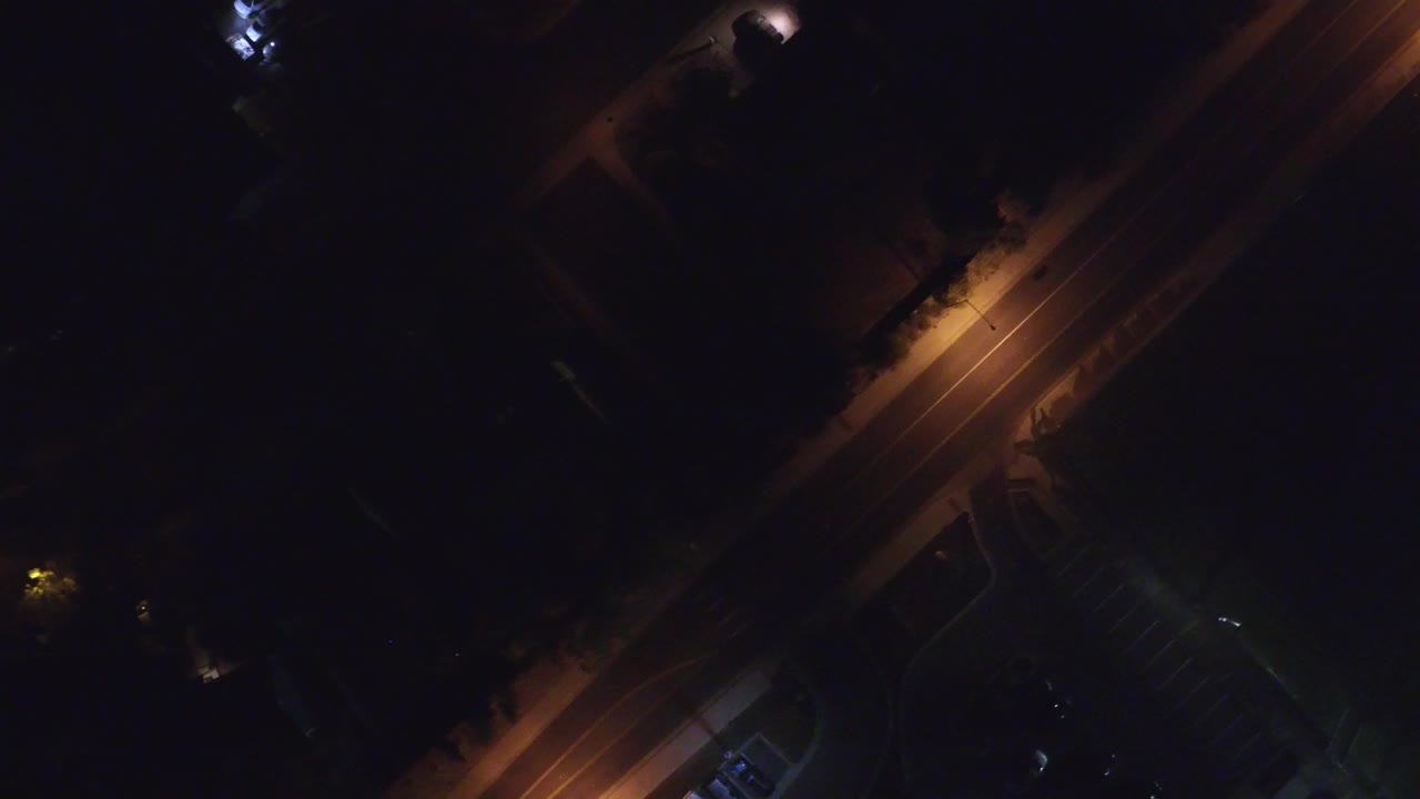 Overhead night frame from Hidden Lake, Colorado showing a diagonal road under warm street lamps, dark surrounding lots, and no visible people.