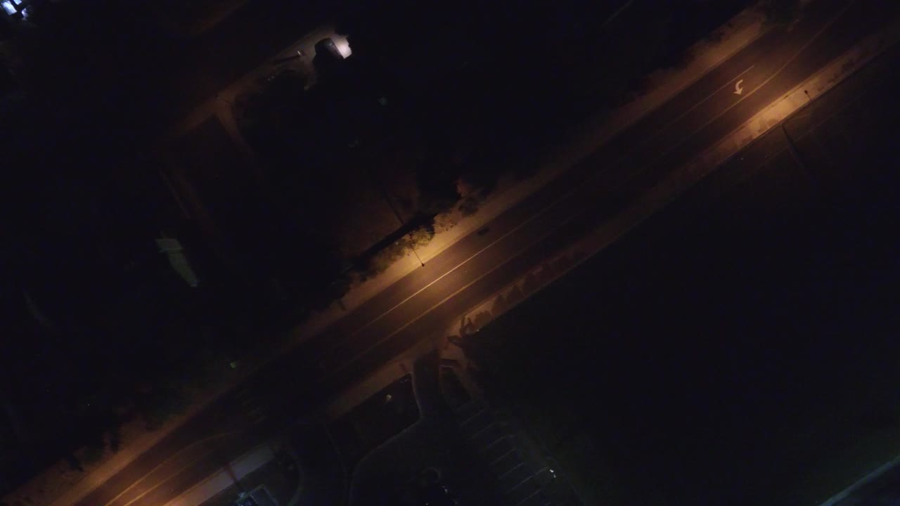 Overhead night frame in Hidden Lake, Colorado showing an empty diagonal street lit by amber streetlights, with dark lots and no visible people.