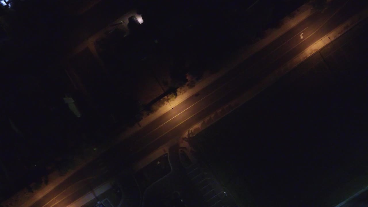 Aerial night view in Hidden Lake, Colorado with the empty street crossing diagonally and a bright streetlight spot near the upper road edge, no visible people.