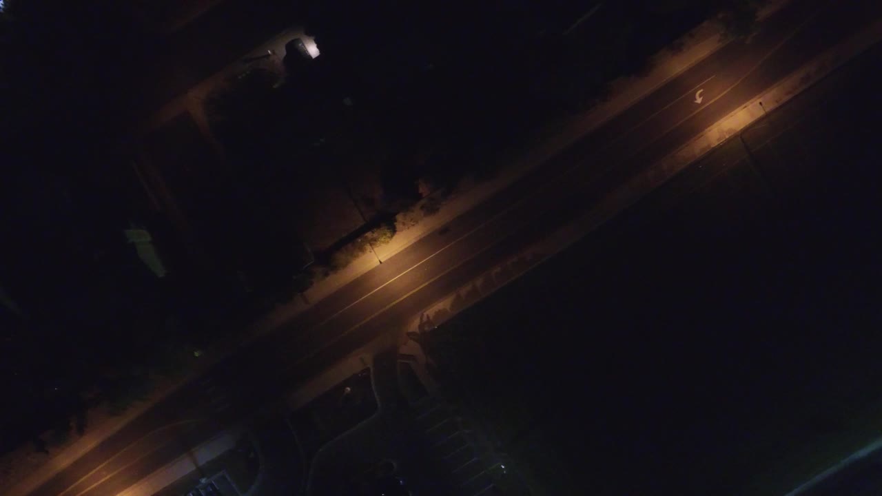 Top-down night street scene with a warm light pool and dark surroundings.