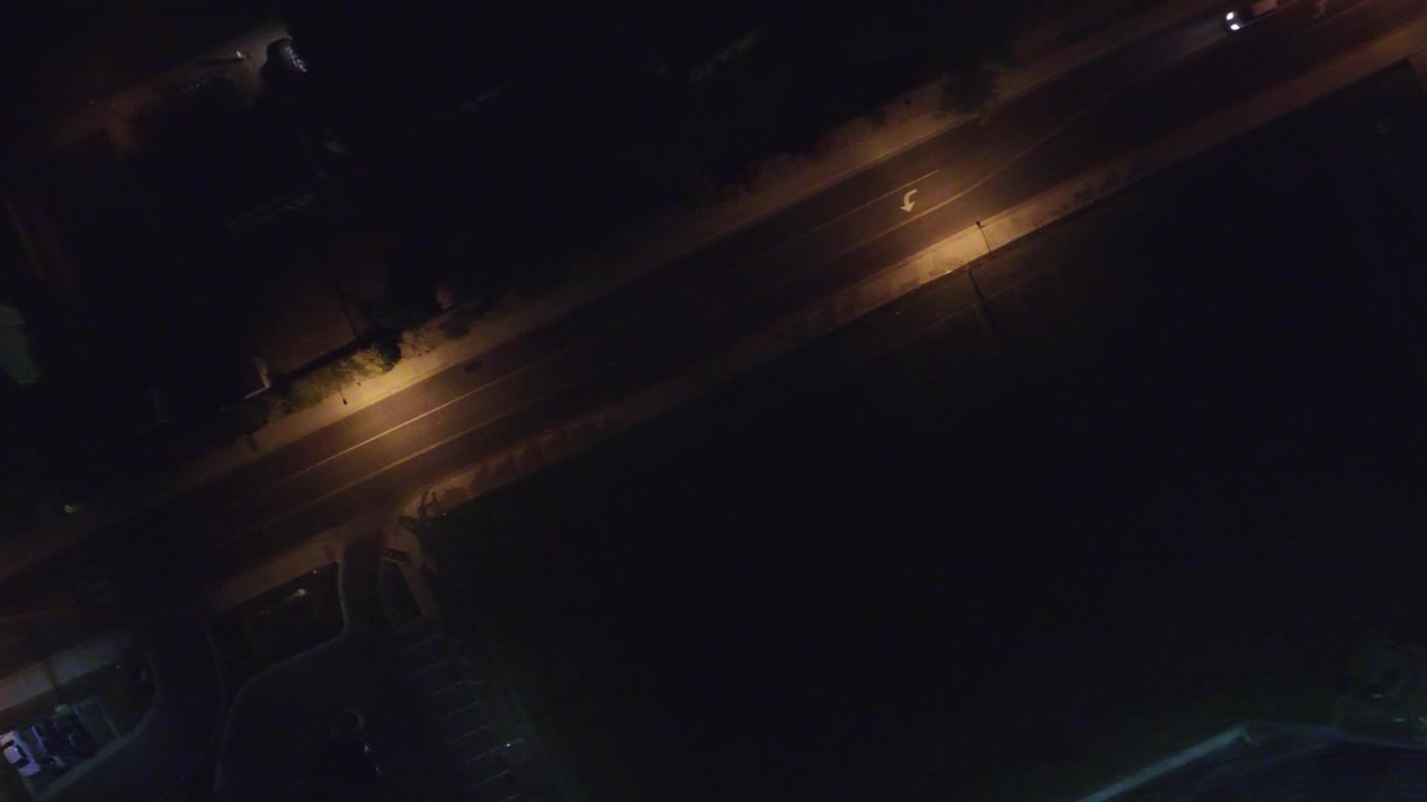 Overhead night view of a diagonal road in Hidden Lake, Colorado with warm street lamps, deep surrounding shadows, and no visible people.