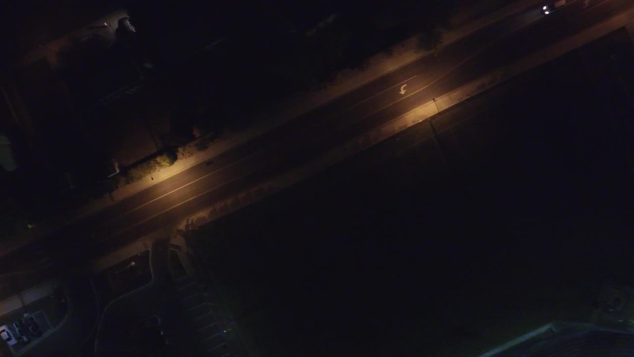 A high night aerial over Hidden Lake, Colorado shows the lamp-lit road near the top of frame and dark paved areas below, with no visible people.
