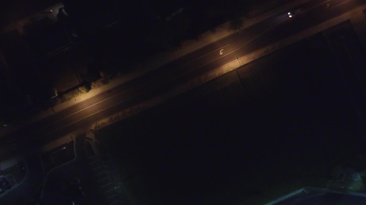 Lamp-lit road at night with a small bright vehicle near the upper right.