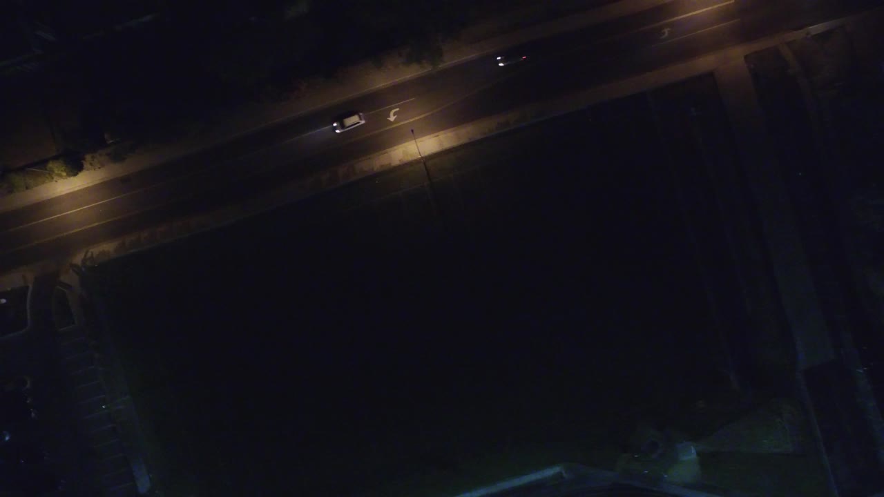 Second overhead frame in Hidden Lake, Colorado with two vehicles on the lit avenue, a large dark structure below the road, and no visible people.