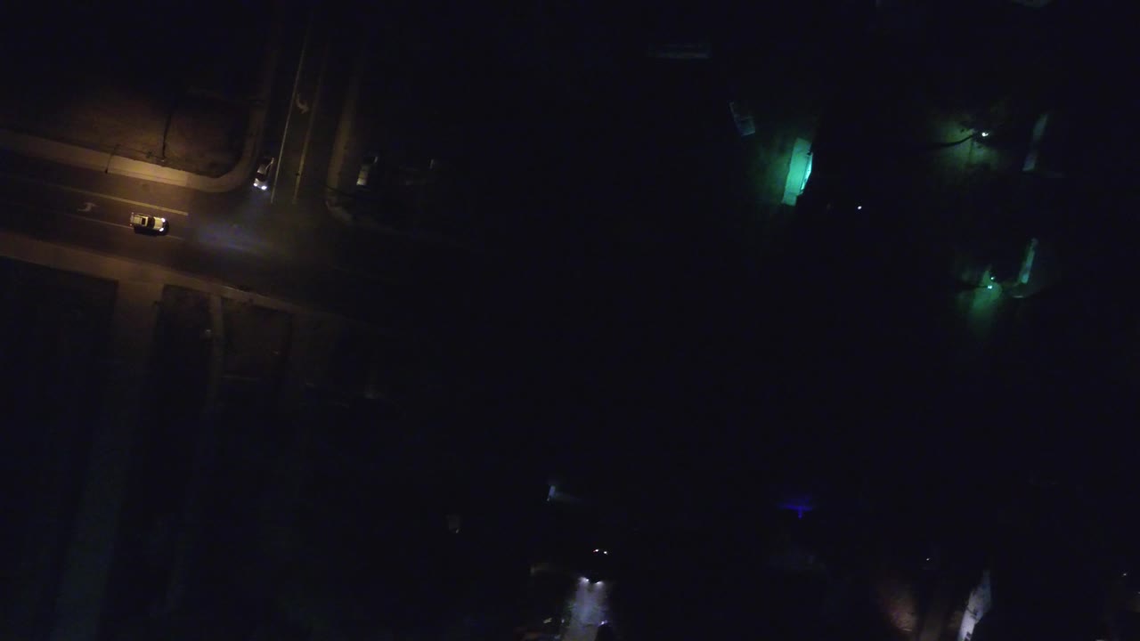 Dark overhead street with warm road lights and faint colored glows.