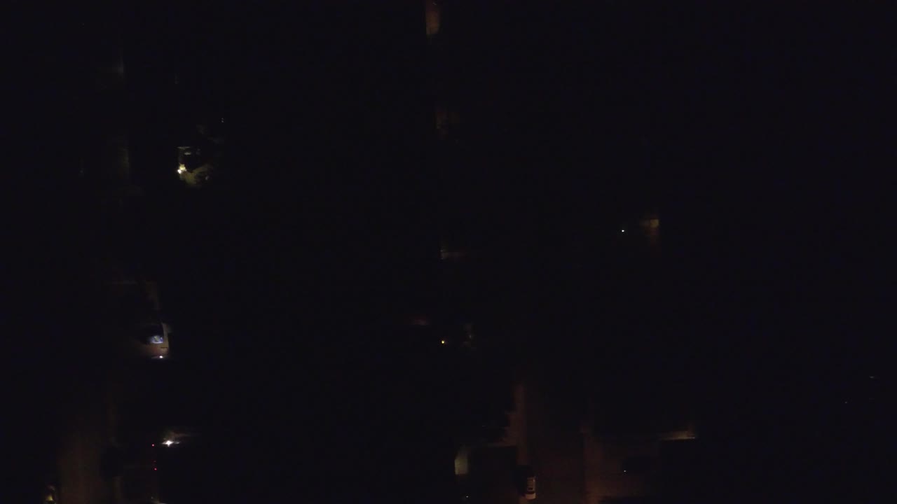 Aerial night frame in Hidden Lake, Colorado, showing isolated lamps and dim roof or driveway shapes against deep shadow, with no visible people.