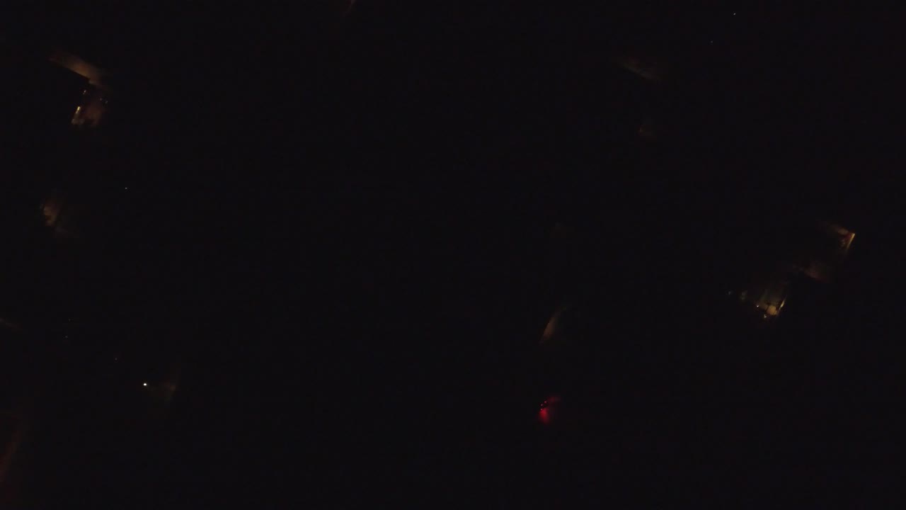Very dark aerial night frame from Hidden Lake, Colorado with a few warm light clusters and tiny white points, no visible people.