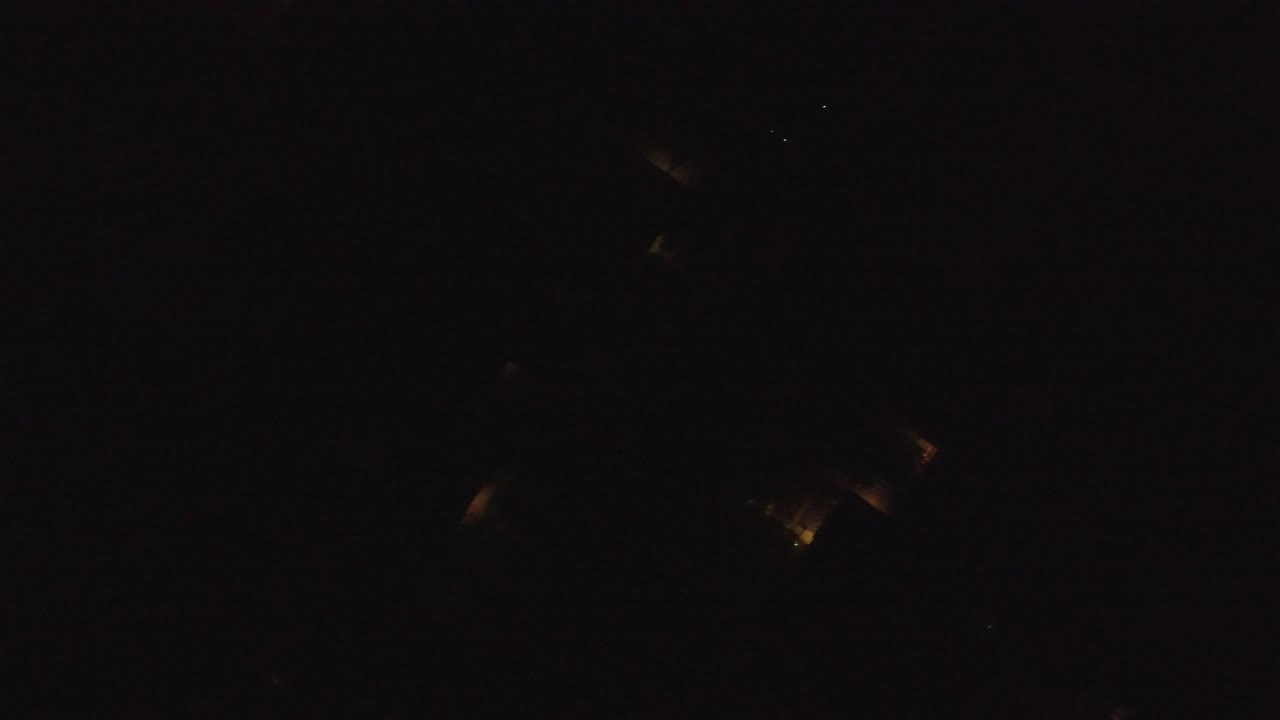 Opening frame of a very dark aerial view over Hidden Lake, Colorado, with faint amber light clusters and no visible people.