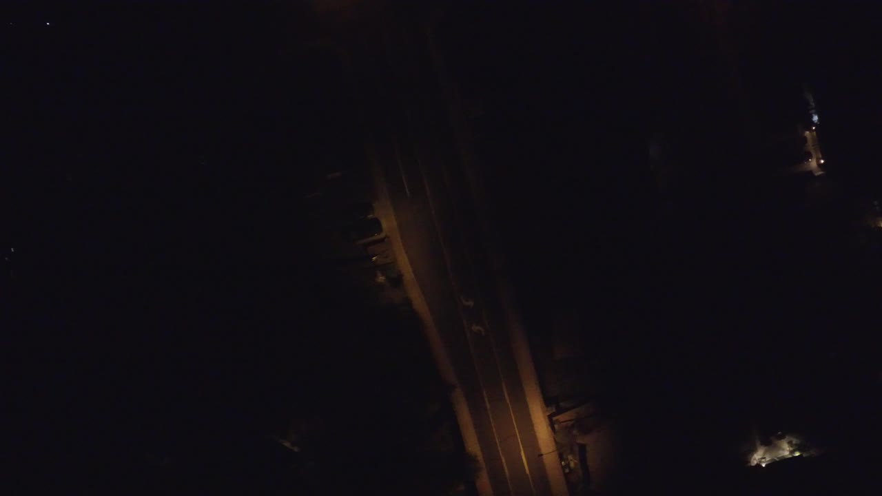 Aerial night frame over Hidden Lake, Colorado showing the street shifted slightly in view, with amber pavement lighting, small illuminated structures, and no visible people.